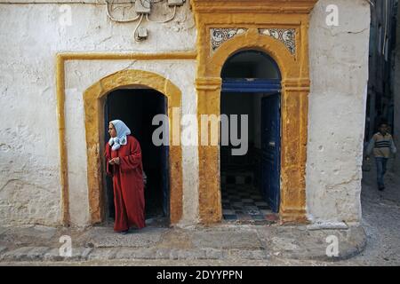 Donna tradizionalmente vestita lasciando per la strada. Città vecchia medina di Essaouira, Marocco. La città vecchia medina è elencata nella lista del Patrimonio Mondiale dell'UNESCO. Foto Stock