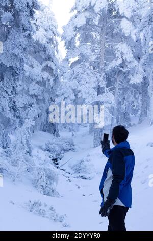 un uomo di mezza età cerca il segnale wifi su una montagna innevata. connessione wifi in natura profonda . Foto Stock