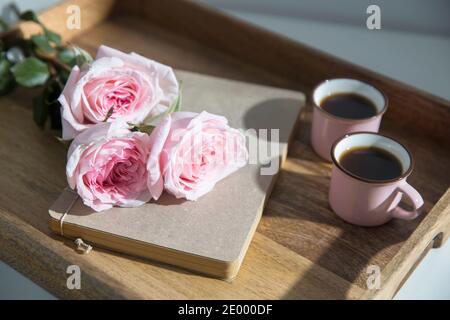 Rosa Bianco Rosa o'hara. Bouquet di rose rosa in vaso di vetro con una teiera bianca e due tazze di cappuccino su un vassoio su un tavolino tra i libri. Foto Stock