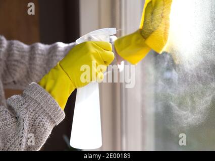 Pulizia di una finestra con detergente spray, guanti in gomma gialla e panno per stoviglie sulla superficie di lavoro per il concetto di igiene, business e salute Foto Stock