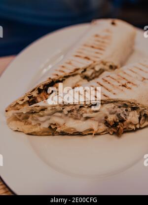 shawarma burito kebab con salsa succulenta ripieno avvolto in pita alla griglia giace su un piatto bianco. delizioso e salutare spuntino appetitoso. natia Foto Stock