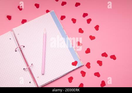 Taccuino vuoto aperto con penna e piccoli cuori su sfondo rosa . Business, scuola e il modello di giorno di San Valentino mock up può essere aggiunto il tuo testo. Foto Stock