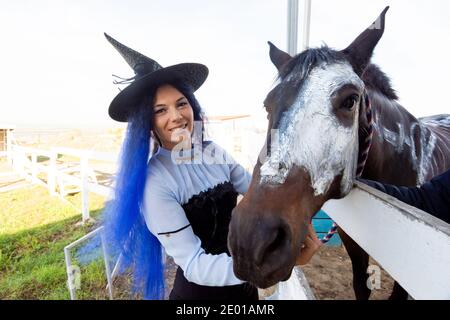 Una ragazza vestita da strega mostra il volto di un cavallo dipinto con vernice bianca per la vacanza di halloween Foto Stock