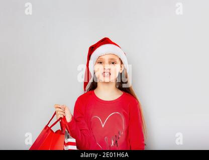 Felice ragazza stanca di capretto che tiene i sacchetti di shopping e gnashing dei denti su sfondo blu con spazio di copia vuoto. Buone feste di Capodanno. Verticale Foto Stock