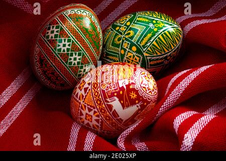 Vacanze di primavera, ingredienti naturali e concetto di pasqua felice con tre uova tinte in un rustico panno rosso vintage con ogni uovo di diverso complesso Foto Stock