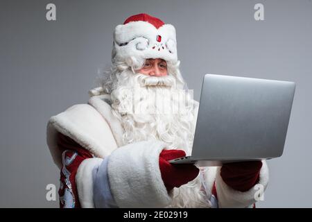 Babbo Natale maschio con i capelli grigi e il laptop in grigio sfondo studio con spazio di copia per la pubblicità di natale nuovo anno Foto Stock