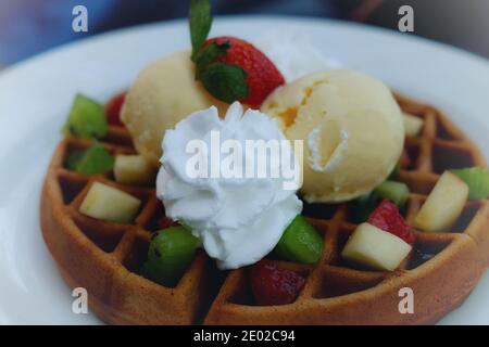 Un piatto di dessert sano contenente un waffle rotondo servito con icecream, panna frusta e frutta sminuzzata assortita. Foto Stock