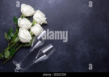 Bouquet di fiori di rose bianche, bicchieri di champagne su sfondo di pietra nera biglietto d'auguri romantico spazio copia Vista dall'alto Foto Stock