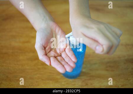 Una donna che stringe una bottiglia chiara di gel antibatterico blu su un tavolo di legno per pulire le mani. Foto Stock