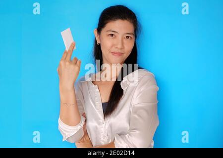 Una donna asiatica attraente fiduciosa che tiene la sua carta di credito, sorridente, preparandosi a fare acquisti con fondo azzurro chiaro chiaro chiaro. Foto Stock