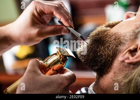 Barber funziona con un regolabarba. Cliente hipster ottenere haircut. Mani di un parrucchiere con regolabarba, closeup Foto Stock