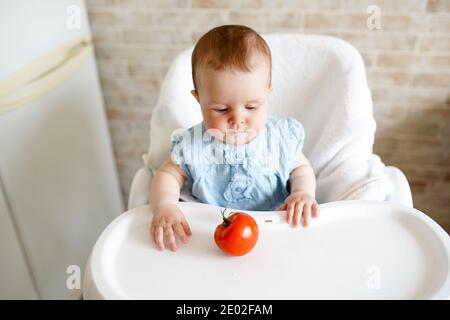 cibo sano per i bambini. Adorabile bambino seduto in sedia e giocando con le verdure. Piccola ragazza mangiare pomodoro. Foto Stock