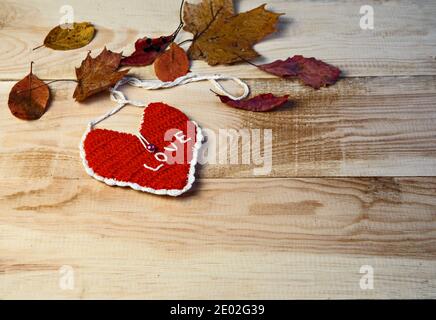 Cuore rosso e foglie marroni d'autunno giacciono su tavola di legno. Messa a fuoco selettiva Foto Stock