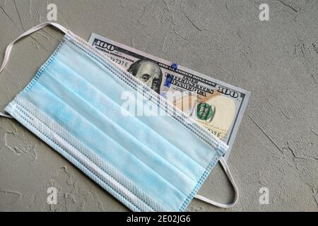 Una fattura di cento dollari e maschere mediche blu su tavola grigia. Foto Stock