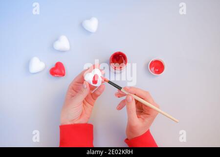 Le mani della donna dipingendo cuori decorativi in rosso. Preparazione per San Valentino. Foto Stock