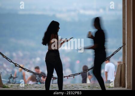 Due ragazze che sono occupate con i loro smartphone dentro Fronte di una catena e Open Urban Landscape e altro Persone in background Foto Stock