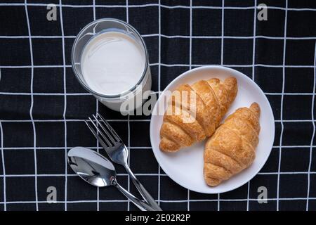 Deliziosi croissant freschi e latte di soia in piastra su sfondo nero con motivi di Plaid. Colazione francese. Gustosi croissant con spazio per la copia Foto Stock