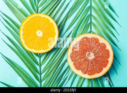 Arance e pompelmo su sfondo colorato. Agrumi a fette di frutta tropicale su foglie di palma. Estate, sole e tropici concetto. Foto Stock
