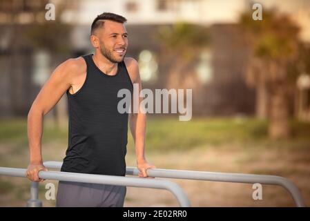 Giovane uomo sportivo che fa i triceps tuffa sulle barre parallele all'aperto. Fare esercizi su barre parallele nel parco Foto Stock