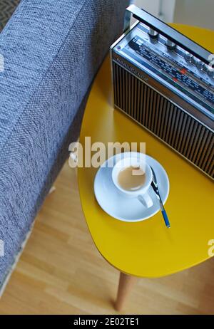 Tazza espresso su un tavolo giallo accanto a un divano e. una radio vintage Foto Stock