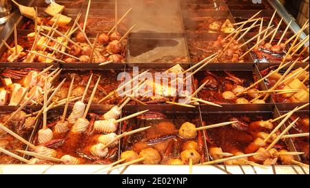 Vari tipi di cibi oden sono cucinati in una pentola piccante divisa in griglie con palle, tofu, bastoncini di pesce e peperoncino. Cucina giapponese in Cina. Foto Stock