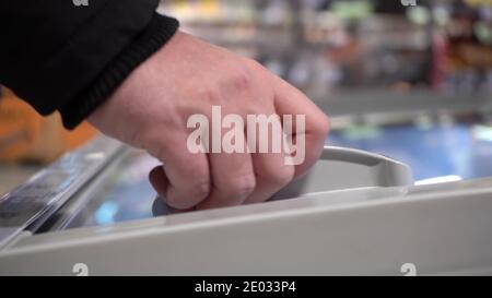 Aprire il congelatore con alimenti surgelati nel supermercato. Tirare indietro il coperchio per prelevare il prodotto congelato. Primo piano. Messa a fuoco selettiva. Concetto di shopping Foto Stock