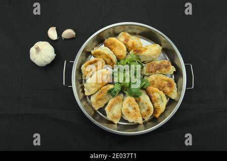 Vista dall'alto di adesivi fritti, gnocchi e sedano in una padella, sfondo nero Foto Stock