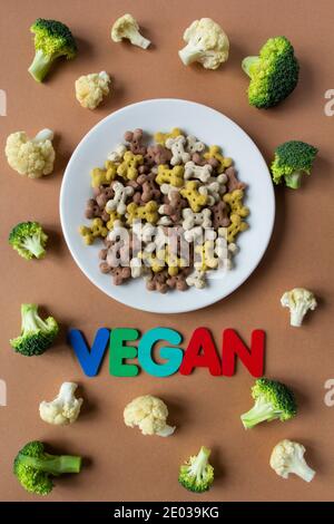 Croccini secchi vegetariani del cane su piatto e verdure su sfondo beige con scritta VEGAN. Foto Stock