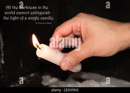 Un uomo che illumina una candela con la citazione di San Francesco d'Assisi. Foto Stock
