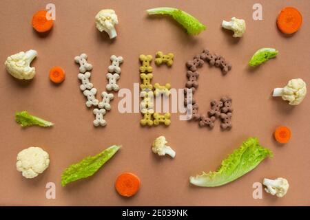 Croccini secchi vegetariani del cane in forma di osso con verdure su sfondo beige. VENG. Scritta Foto Stock