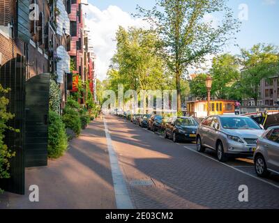 Amsterdam, Paesi Bassi - Giugno 2019. Una stretta strada cittadina con auto parcheggiate sul lato di una strada Foto Stock