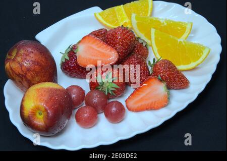 Frutta varia su piatto bianco, piatto di frutta, fragole, nettarine, arance e uva Foto Stock