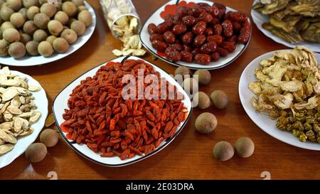 Bacche di Goji, longani secchi, datteri rossi su tavolo di legno, vista dall'alto, erbe cinesi, supplemento dietetico Foto Stock