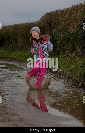 Giovane ragazza felice che salta in puddddle fangose. Inghilterra Foto Stock