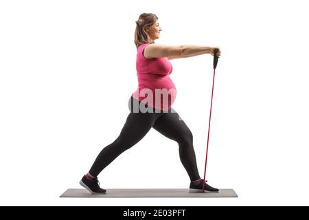 Foto di profilo di lunghezza completa di una donna incinta che si esercita con una banda yoga su un tappetino isolato su sfondo bianco Foto Stock