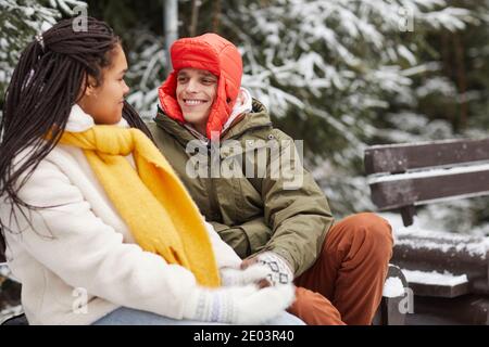 Felice giovane che sorride alla donna durante la conversazione la panchina nel parco invernale Foto Stock