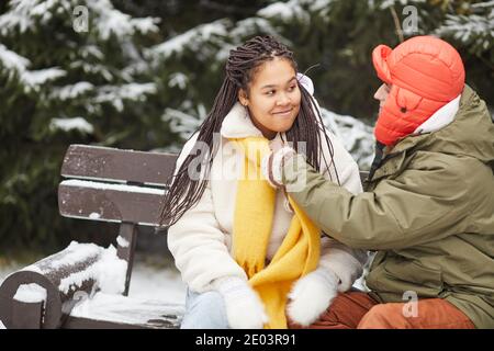 Giovane uomo che indossa una sciarpa calda sul collo della sua fidanzata prima la loro passeggiata nel parco in inverno Foto Stock