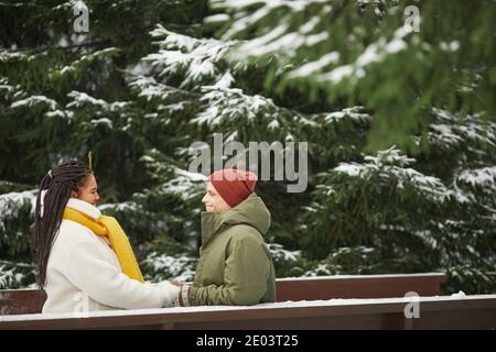 Giovane coppia in abiti caldi seduti l'uno di fronte all'altro date romantiche all'aperto con abeti innevati nel sfondo Foto Stock