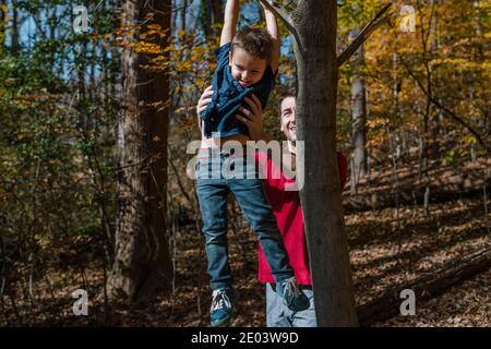 Papà che aiuta il figlio a salire un albero nella giornata di sole Foto Stock