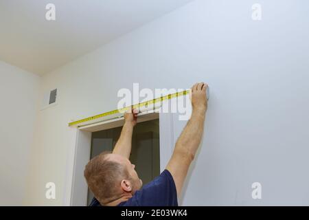 Falegname che misura la lunghezza della modanatura sulle porte, montando sul rivestimento del telaio Foto Stock
