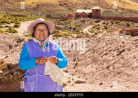 Vecchia signora di San Pedro de Atacama tessitura a mano e posa di fronte alla sua casa. Deserto di Atacama, Cile Foto Stock