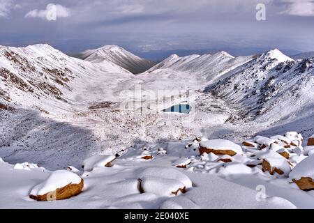 Epica vista mattutina di una valle montana con laghi morenici dopo una notte di nevicata; la prima neve in montagna con l'avvicinarsi del mare invernale Foto Stock