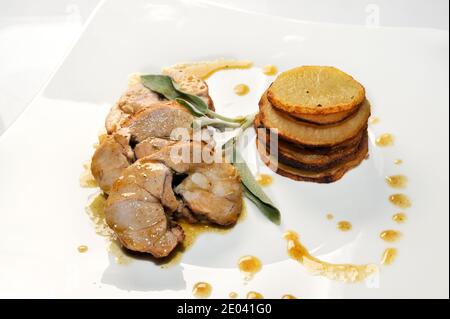 involtini di coniglio arrosto, fette di salsa e patate e foglie di salvia in piatto bianco Foto Stock