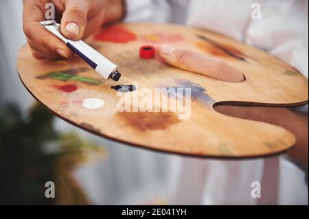 Mano dell'artista che strizza la vernice dell'olio dal tubo dentro la tavolozza Foto Stock