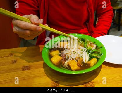 Una donna che mangia un pasto di un piatto di patate, carne, pesce e verdure con chopsticks, Vietnam, Asia Foto Stock