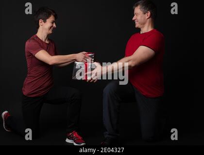 Coppia Personal Trainer che consegna una confezione regalo avvolta in lamina d'argento e nastro rosso. Foto Stock