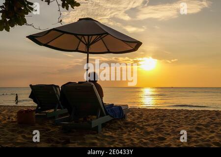 Una donna matura seduta sotto un ombrellone o un'ombra sulla spiaggia guardando il tramonto, Phu Quoc, Vietnam, Asia Foto Stock