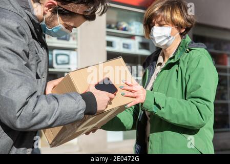 Uomo di consegna indossando una maschera e un pacchetto consegnato alla donna con una maschera, mantenere la distanza sociale Foto Stock