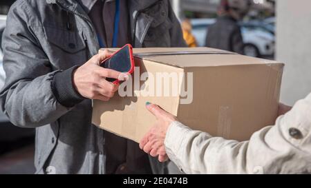 Uomo di consegna con il telefono cellulare in mano mani su un box alla donna Foto Stock