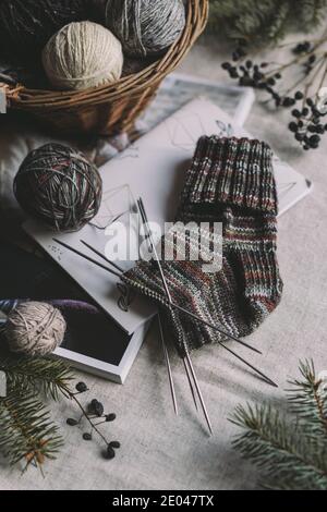 Calzino per maglieria a mano con aghi e palle di filato in un cestello. Concetto per la vita lenta fatta a mano e hugge. Foto Stock